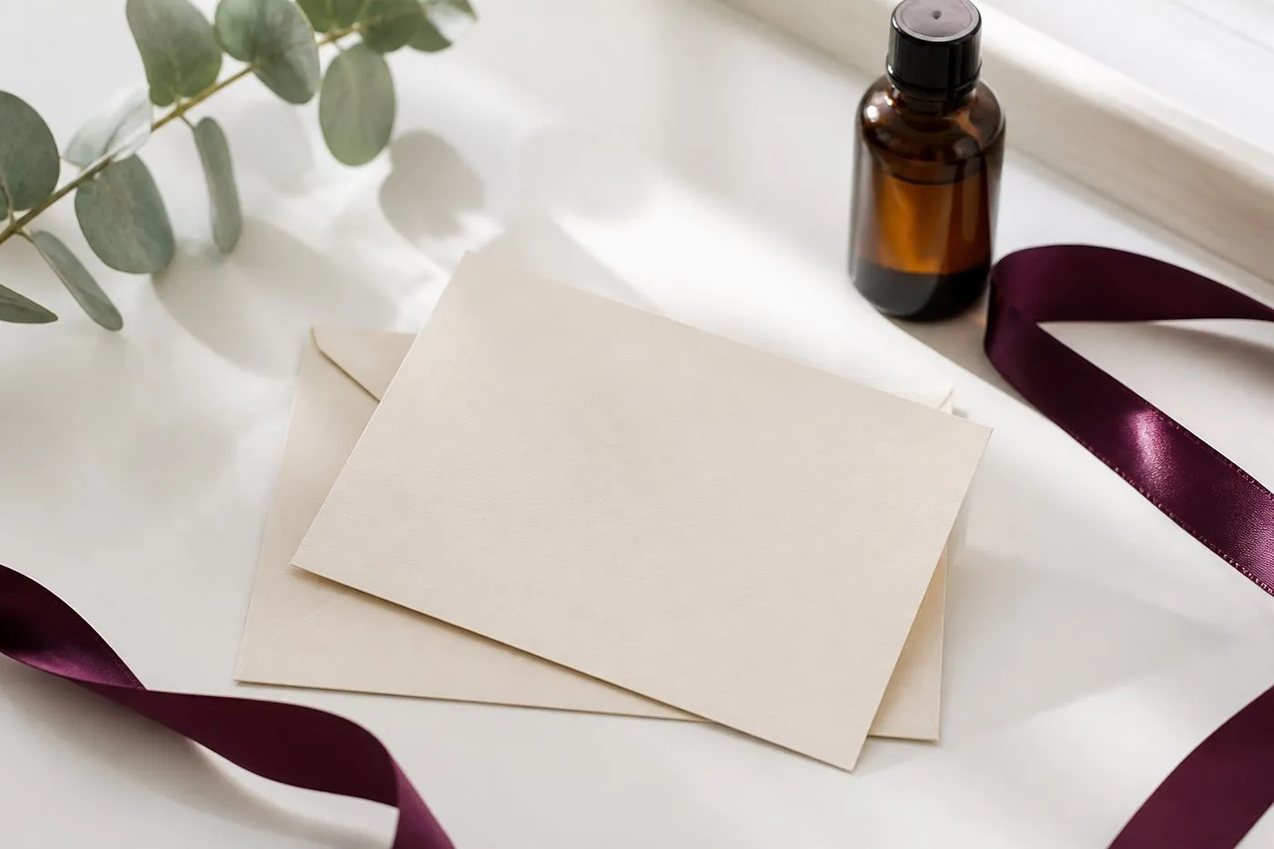 Une carte crème et son enveloppe, un ruban de satin prune et un flacon de soin